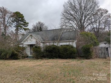 Shows the exterior of a one story home with an overgrown yard and peeling paint at 2801 Pennsylvania Ave, Kannapolis, NC 28083