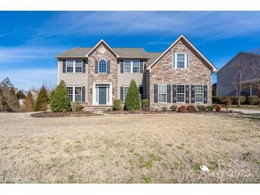 Charming two-story home featuring a stone and vinyl facade, black shutters, and a well-manicured front yard at 8471 Penton Pl, Harrisburg, NC 28075
