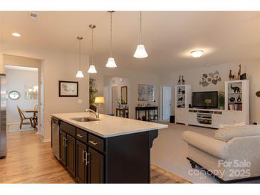 Open-concept kitchen featuring an island with pendant lighting and stainless steel appliances, flowing into the living area at 3156 Pinehills Way, Mount Holly, NC 28120