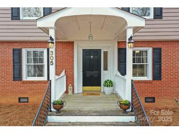 Charming brick home featuring a welcoming front porch with elegant railing, and a black front door at 305 Wagner St, Troutman, NC 28166