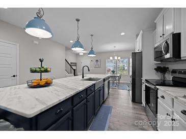 An open kitchen features a large center island with a marble countertop and modern blue pendant lighting at 201 Bennett Trail Dr, Mount Holly, NC 28120