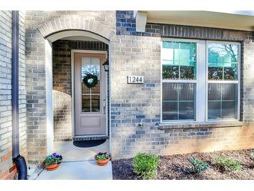 Charming brick home featuring a welcoming arched entryway, decorative wreath, and vibrant potted flowers at 1244 Madison Towns Ln, Charlotte, NC 28209