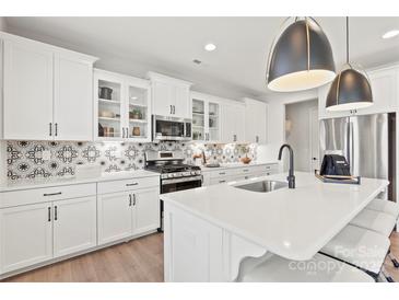 Well-lit kitchen with stainless steel appliances, white cabinets, island with sink, and decorative backsplash at 5009 Duval Cir, Tega Cay, SC 29708