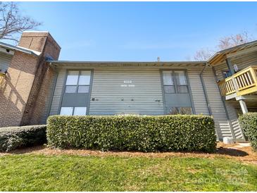 Exterior shot of condo building with light gray siding, green grass, and trimmed bushes under a clear blue sky at 4918 Sardis Rd # E, Charlotte, NC 28270