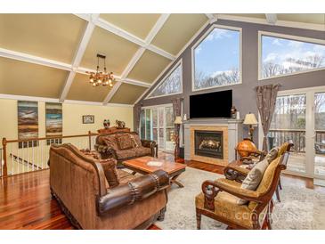 Bright living room featuring vaulted ceiling, fireplace, large windows, hardwood floors, and comfortable seating at 108 Outside Loop Ln, Mooresville, NC 28117