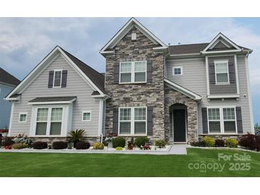 Charming two-story home featuring a stone facade, gray siding, manicured lawn, and professional landscaping at 7133 Sumters Camp Trl, Fort Mill, SC 29707