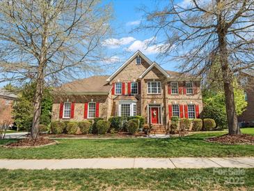 Charming two-story brick home featuring a manicured lawn, red shutters, mature trees, and a welcoming red front door at 2907 Blackburn Dr, Waxhaw, NC 28173