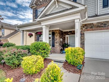 Charming brick home featuring a landscaped front yard and covered porch with hanging flower baskets at 2033 Folkstone Ln, Indian Land, SC 29720
