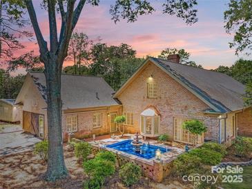 Stunning brick home featuring a unique water feature, lush greenery, and mature trees creating a private outdoor oasis at 1359 Carmen Ln, Gastonia, NC 28054