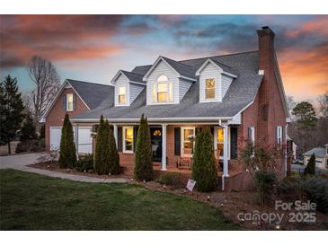 Charming brick home featuring a cozy front porch, lush lawn, and mature evergreen trees at 6068 Gold Creek Estate Dr, Hickory, NC 28601