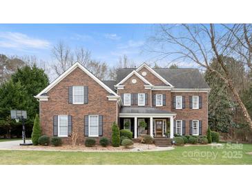 Imposing two-story brick home featuring symmetrical design, black shutters, mature landscaping and covered entryway at 518 Streamside Ln, Marvin, NC 28173