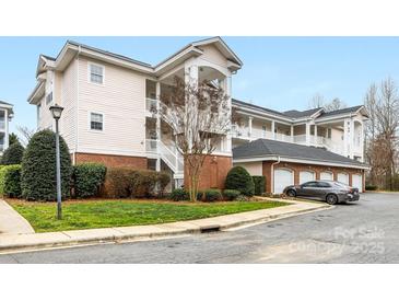 Condominium exterior featuring manicured lawn and landscaping, brick accents, covered balconies, and private garages at 8759 Coralbell Ln, Charlotte, NC 28213