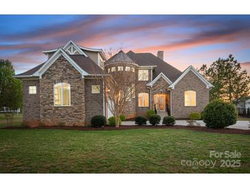 Stunning brick home with turret, manicured lawn, and professional landscaping at sunset at 121 Dabbling Duck Cir, Mooresville, NC 28117