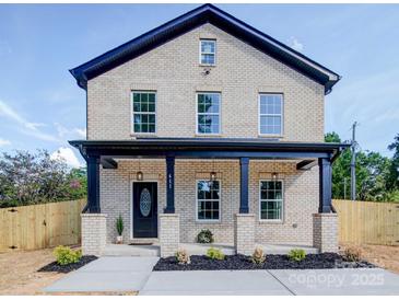 Charming brick home boasts a welcoming front porch, complemented by dark blue accents and meticulous landscaping at 588 Washington Ln, Albemarle, NC 28001