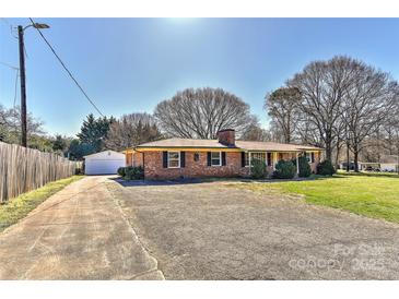 Charming brick ranch-style home with a detached garage, and spacious front yard on a sunny day at 1356 Ford Dr, Lowell, NC 28098