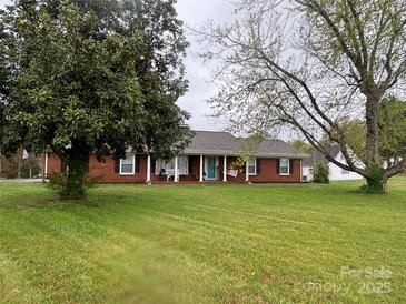 Charming brick home featuring a covered porch and a spacious front yard with mature trees, set against a cloudy sky at 30 Hillsboro Rd, Taylorsville, NC 28681