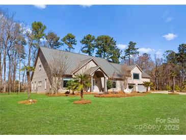 Expansive brick home featuring mature trees, a metal roof, and a well manicured lawn under a bright blue sky at 16455 Harbor View Rd, Charlotte, NC 28278