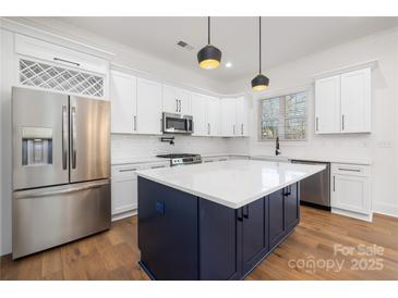 Modern kitchen featuring stainless steel appliances, white cabinets, and a contrasting dark blue island with a white countertop at 302 Lincoln St, Belmont, NC 28012