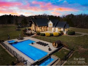 A dusk aerial view of a backyard pool area, including a hot tub, sauna, lounge chairs, and waterfall feature at 12613 Oak Grove Rd, Stanfield, NC 28163
