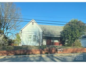 Modest one-story home with white siding, brick foundation and mature tree on a sunny day at 107 N Market St, Lancaster, SC 29720