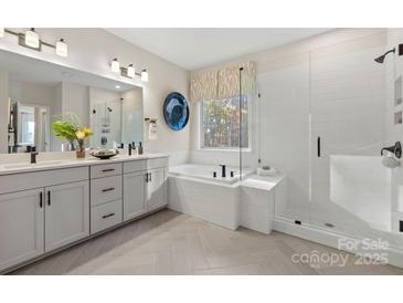 Bright bathroom with white cabinets, dual vanity, tub, and glass shower featuring black hardware and herringbone tile floors at 164 Holsworthy Dr, Mooresville, NC 28115