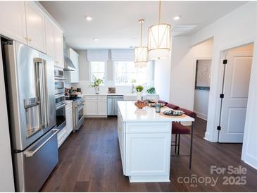 Bright kitchen features white cabinetry, stainless steel appliances, pendant lighting, and a spacious center island with seating at 317 Old Town Village Rd, Waxhaw, NC 28173