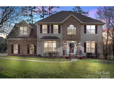 Charming two-story home featuring a brick facade, manicured lawn, and inviting entryway with red shutters and flower pots at 7510 Plumcrest Ln, Harrisburg, NC 28075