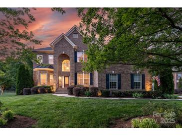 Elegant brick home with manicured lawn, lush landscaping and a picturesque sunset backdrop at 3017 Chisholm Ct, Waxhaw, NC 28173