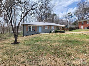 Charming one-story home with a metal roof, baby-blue door, brick facade, and an established yard at 112 Greentree Dr, Mount Holly, NC 28120