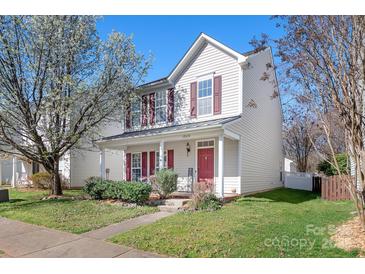 Charming two-story home with red shutters and a welcoming front porch surrounded by lush greenery and blooming trees at 12419 Swan Wings Pl, Huntersville, NC 28078