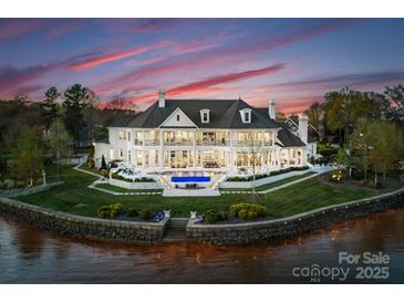 Expansive waterfront estate features a private pool, lush landscaping, and stunning architectural details at sunset at 8228 Bay Pointe Dr, Denver, NC 28037