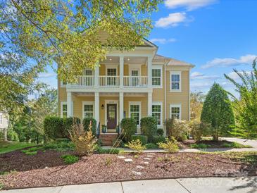 Charming yellow two-story home with white pillars, balcony, landscaped yard and inviting front porch at 2009 Waterbury Ln, Waxhaw, NC 28173
