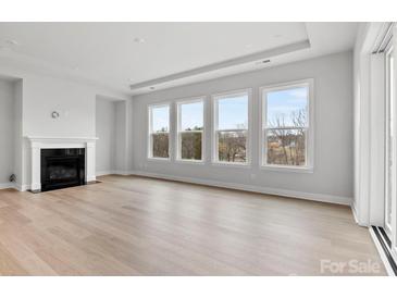 Bright, neutral living room featuring a fireplace, hardwood floors, and large windows offering natural light and treetop views at 3050 Tramore Dr, Harrisburg, NC 28075