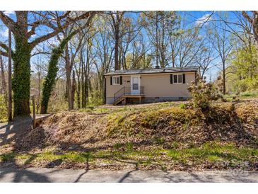 Tan home with black trim situated on a beautiful tree-filled lot with a small front porch at 216 E Georgia Ave, Bessemer City, NC 28016