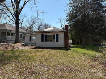 A small one-story home has light siding with blue shutters, and a brick chimney in a yard of dead grass at 1407 Birch St, Kannapolis, NC 28081