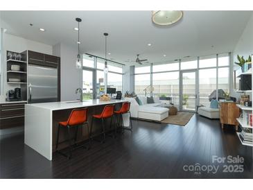 Open-concept living room with dark wood floors, modern kitchen island, and bright natural light from the large windows at 1100 Metropolitan Ave # 314, Charlotte, NC 28204