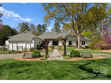 Beautiful front exterior of home with lush lawn, a vine covered pergola, seating, and mature trees at 2015 Pellyn Wood Dr, Charlotte, NC 28226