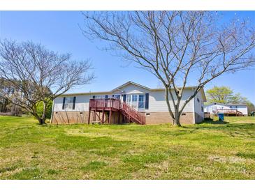 View of home exterior with lawn, mature trees, deck, and blue sky background at 216 Sylvan Rd, China Grove, NC 28023