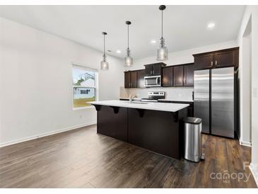 This kitchen features an island, stainless steel refrigerator, hardwood floors, and modern pendant lighting at 1976 Ethan Ln, Stanfield, NC 28163