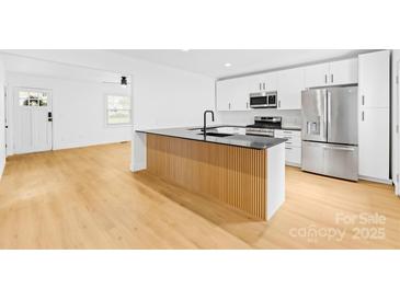 Modern kitchen features a black countertop island with natural wood accent, white cabinetry, and stainless steel appliances at 1409 Effingham Rd, Charlotte, NC 28208