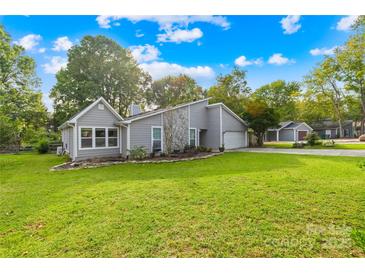 Charming gray house featuring a stone accent wall, green lawn, and mature trees under a bright sky at 6741 Stillmeadow Dr, Charlotte, NC 28277
