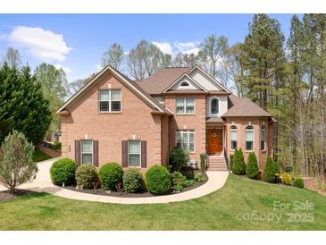 Brick home featuring a well-manicured lawn, mature trees, and a welcoming front entrance at 164 Crooked Branch Way, Troutman, NC 28166