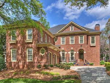 A beautiful red brick home with manicured landscaping, blue sky, and mature tree in this exterior elevation at 8912 Heydon Hall Cir, Charlotte, NC 28210