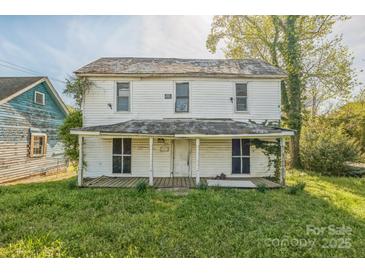 Two-story white home with a covered porch and overgrown landscaping at 303 E Fisher St, Salisbury, NC 28144