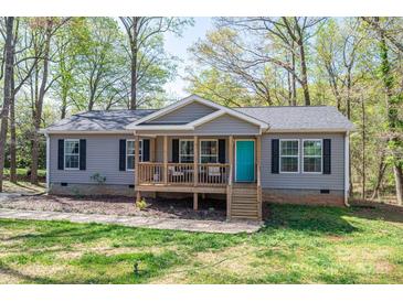 Charming gray home with a wooden porch, a teal front door and beautifully landscaped front yard at 7790 Caswell Rd, Stanley, NC 28164