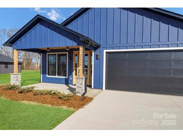 Charming blue home featuring a covered porch with stone accents and a dark gray garage door at 32525 Buchanan Ln, Albemarle, NC 28001