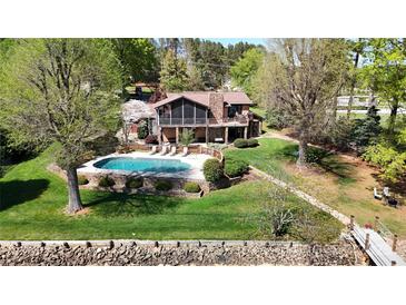 An aerial view of a beautiful stone home with a sparkling pool and a lush green lawn at 7424 Windy Pine Cir, Denver, NC 28037