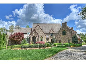 Stunning stone home featuring manicured landscaping and a timeless aesthetic beneath a cloudy, bright blue sky at 1012 Clover Crest Ln, Weddington, NC 28104