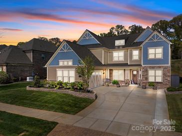 Beautiful two-story home with stone accents, a well-manicured lawn, and a spacious driveway at sunset at 10904 Kilkenny Dr, Matthews, NC 28105