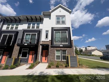 Modern two-story townhome featuring brick accents, a small balcony, an orange front door, and manicured lawn at 648 W End Dr, Charlotte, NC 28208